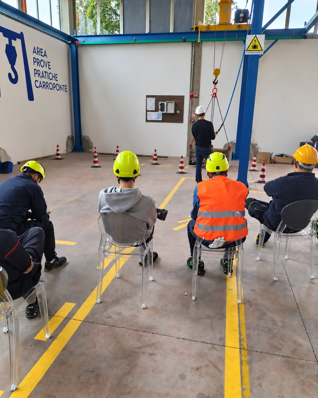 Partecipanti di spalle osservano una dimostrazione in un’area per prove pratiche su carroponte.