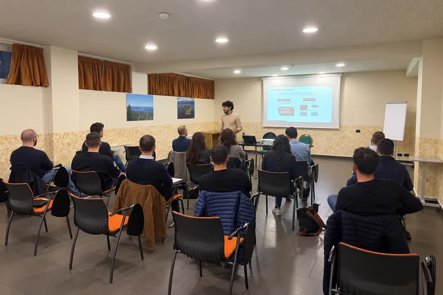 Foto reale ritoccata: docente durante una lezione sul tema antincendio, con i partecipanti rivolti verso di lui.